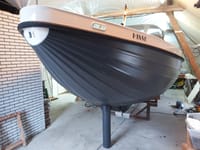 Een tweekleurige boot met de naam "HISSE" op de zijkant en de letters "JH" op de boeg staat binnen op bokken.