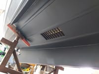 De onderkant van een grijze boot met een rechthoekig rooster is zichtbaar, ondersteund door een roestbruine bok.