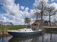 Een blauw-grijze boot met een lichte opbouw en donkere kap ligt in het water, met de naam "HISSE" op de boeg.