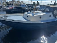 Een blauw-witte boot met de naam "HISSE" op de boeg ligt in het water, met zonnepanelen en een donkere kap.