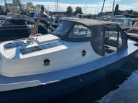 Een wit-grijze boot met een donkere romp, voorzien van een donkergrijze kap, zonnepanelen en twee patrijspoorten.