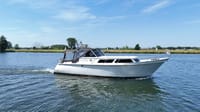 Een witte motorboot met een zwarte kap vaart op een blauwe waterweg onder een heldere hemel. — Valk Sport