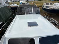 Een witte boot met een zwart dak en een luik op het voordek, omringd door andere boten op het land. — Valk Sport
