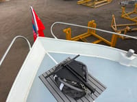 Een zwart anker ligt op een grijze mat op het dek van een boot, met een rode vlag aan de boeg. — Valk Sport
