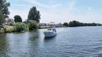 Een witte motorboot vaart op een waterweg met bomen langs de oevers en een jachthaven in de verte. — Valk Sport