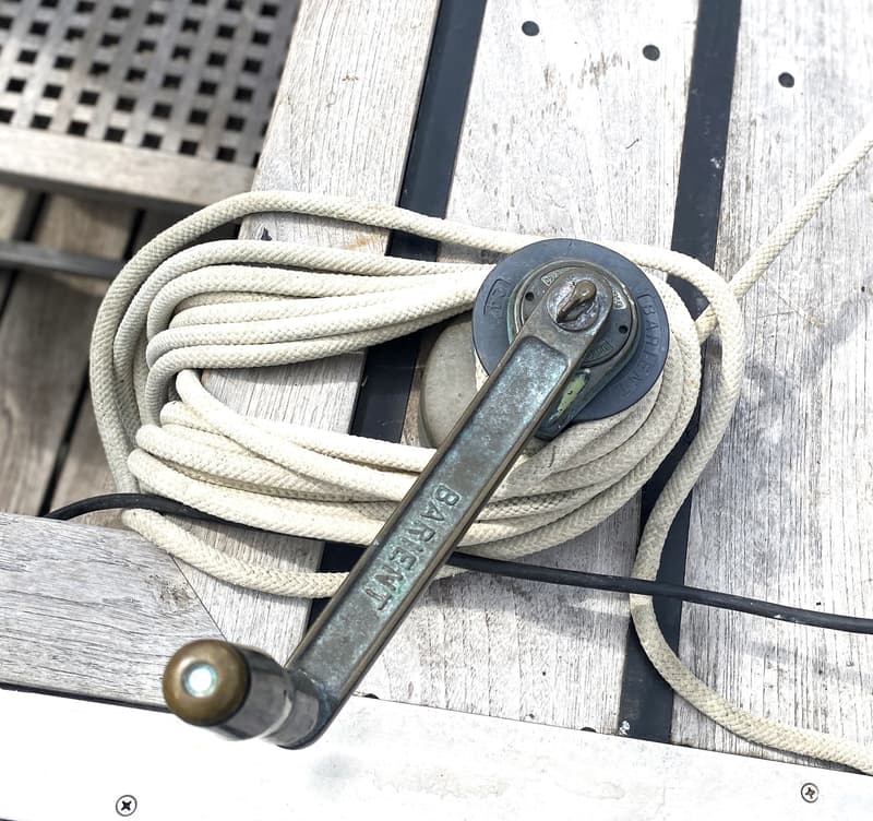 Een lierhendel met "BARIENT" erop, een opgerold wit touw en een lier op een houten dek.
