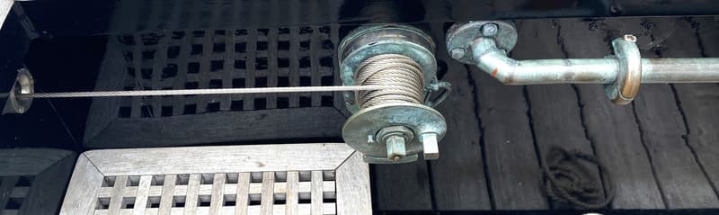 Een detailfoto van een boot met een lier met staalkabel, een metalen stang en een houten rooster. — Schokker 14.00 M. One Off