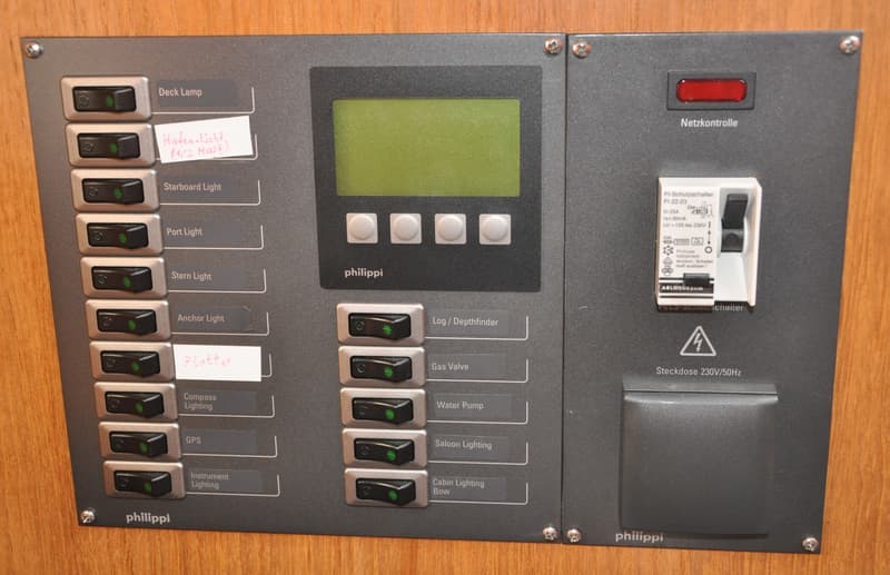 Een grijs bedieningspaneel met schakelaars, een digitaal display, een zekering en een stopcontact, gemonteerd op een houten…