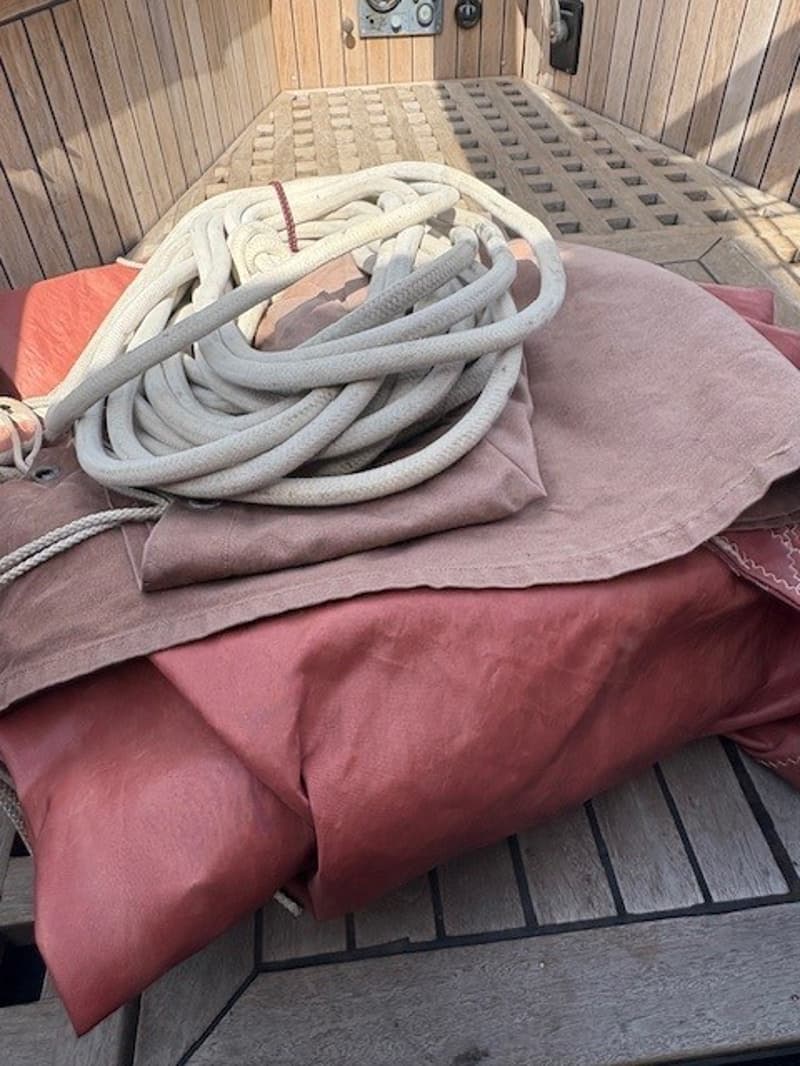 Een opgerolde witte lijn en twee opgevouwen roodbruine doeken liggen op een houten dek.