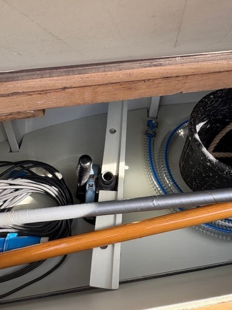 Een detailfoto van een bootinterieur met kabels, slangen, een pomp en houten en metalen stangen.