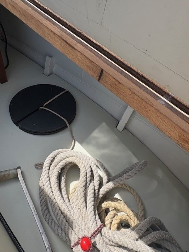 Een opgerolde lijn met een rode boei ligt op een lichte ondergrond naast een houten rand en een zwart rond object.