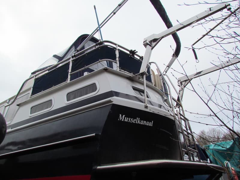 Een zwart-witte boot met de naam "Musselkanaal" op de achtersteven, met een blauwe kap en een stalen davit.