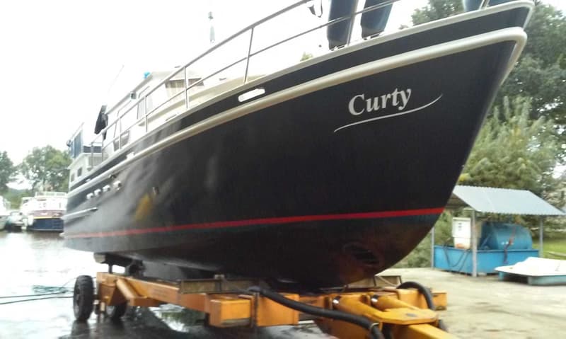 Een donkerblauwe boot met de naam "Curty" in witte letters, staat op een gele trailer op het droge. — Curtevenne 950 GSAK