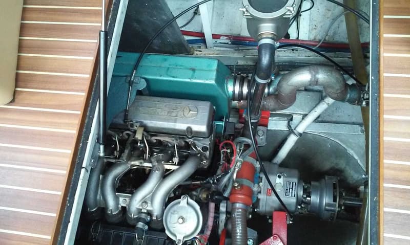 Een Mercedes-Benz scheepsmotor met diverse leidingen en slangen is zichtbaar in een motorruimte met houten afwerking.