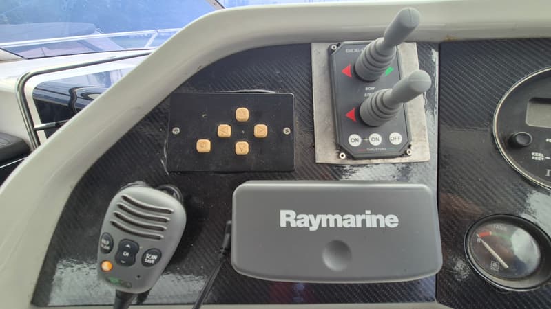Een detailfoto van een bootdashboard met een Raymarine-apparaat, thrusterbediening, een marifoon en een tankmeter.