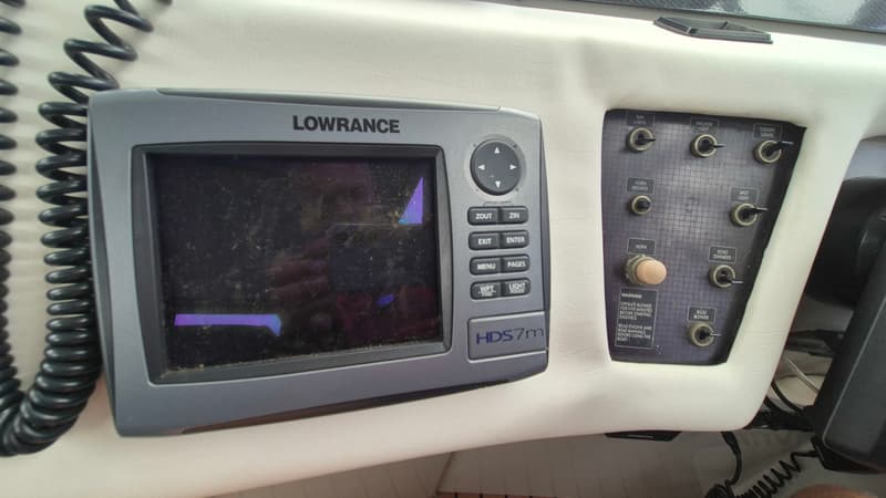 Een Lowrance HDS7m navigatiesysteem en een schakelpaneel met diverse knoppen en een waarschuwingslabel.