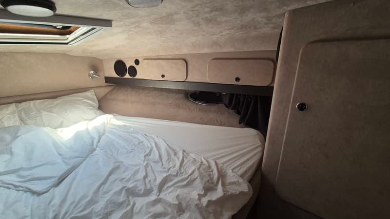 De foto toont een kajuit met een bed met wit beddengoed, opbergvakken, luidsprekers en een dakluik. — Sunseeker 38 Martinique