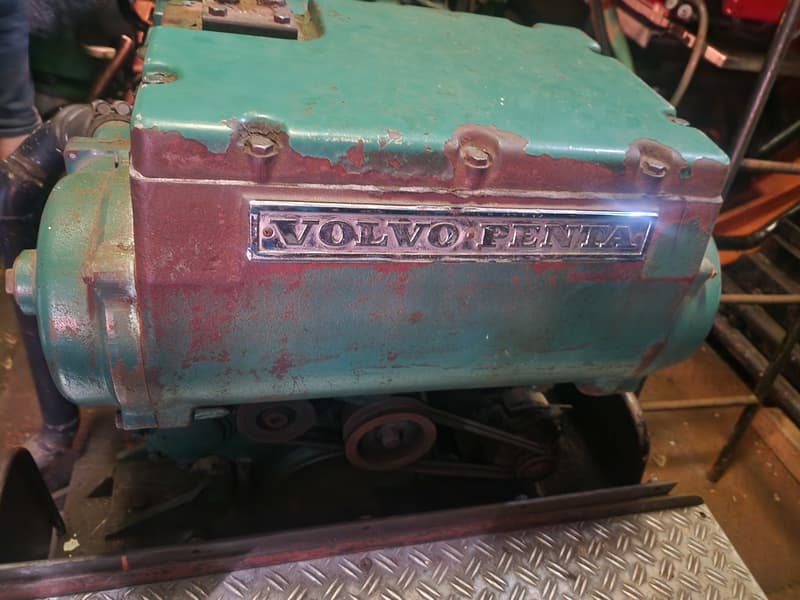 Een close-up van een roestige, groen geverfde Volvo Penta motor met zichtbare riemen en poelies.