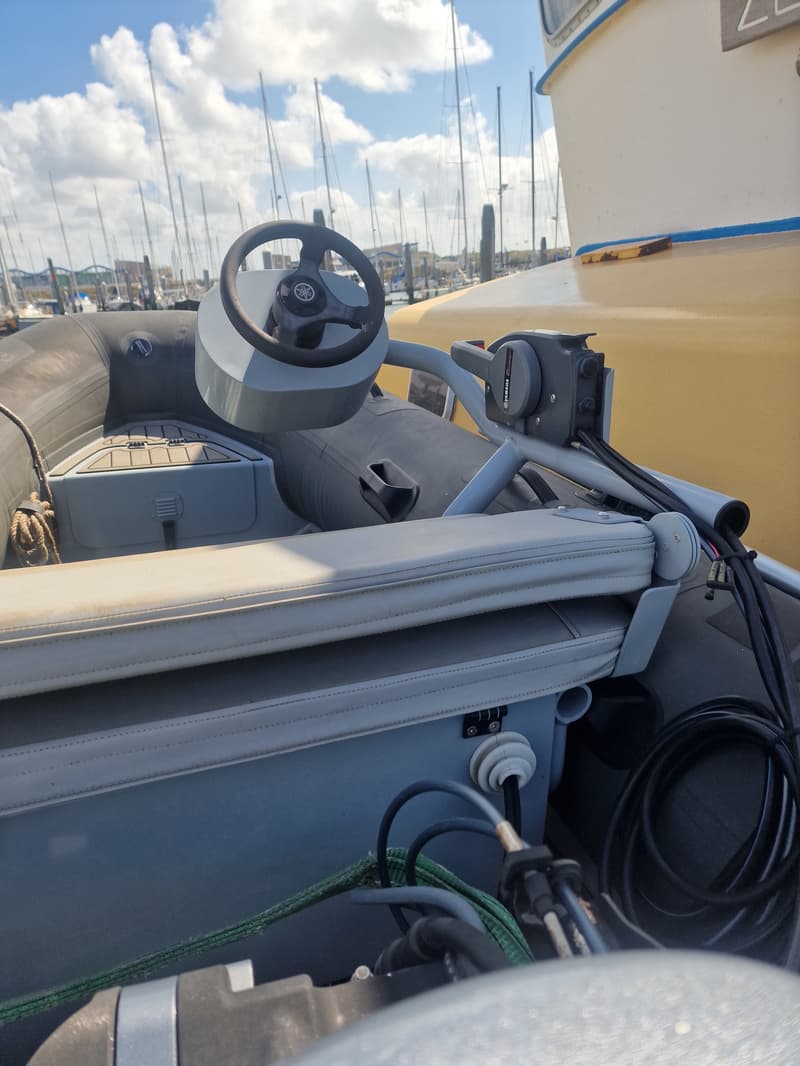 Een stuurwiel met Yamaha-logo en een gashendel in een rubberboot, met een jachthaven op de achtergrond.