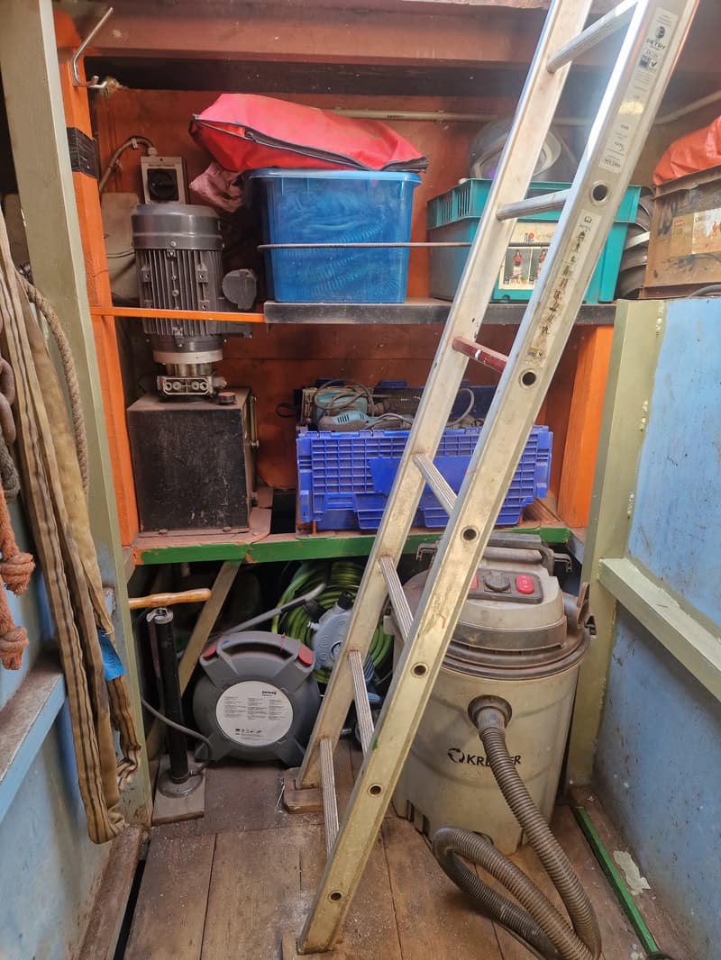 Een opslagruimte met een ladder, gereedschap, kratten en een stofzuiger.