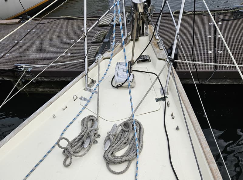 De boeg van een zeilboot met opgerolde lijnen op kikkers en een ankerlier, liggend aan een steiger. — Frans Maas Raider 35