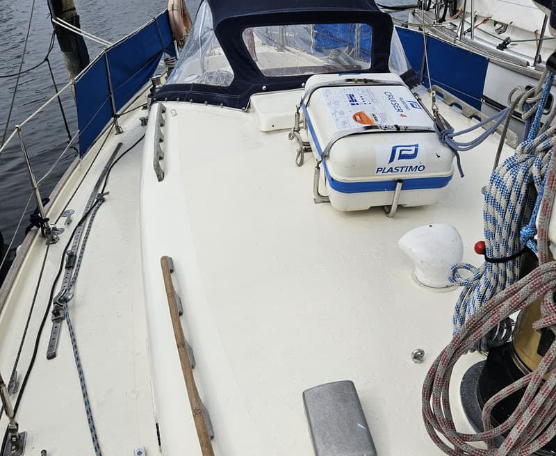 Een bovenaanzicht van het dek van een zeilboot met een reddingsvlot, touwen en een blauwe buiskap. — Frans Maas Raider 35