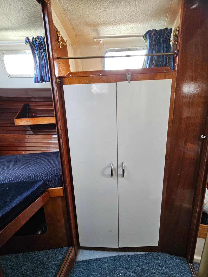 Een interieur van een boot met een witte kast, houten wanden, een blauw tapijt en een bed met blauwe kussens.