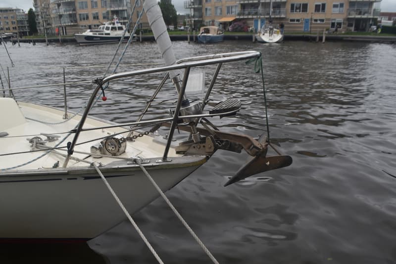 De boeg van een witte zeilboot met een anker en een ankerlier, afgemeerd aan een kade. — Frans Maas Raider 35