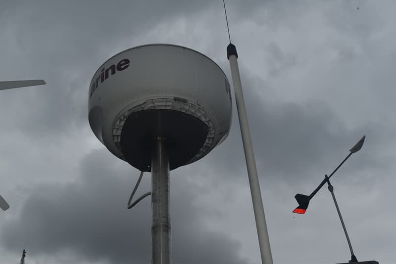 Een witte Raymarine radarbol met een beschadigde onderrand, een antenne en een windvaan met een rood vlak, tegen een…