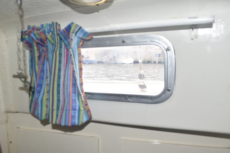 Een kleurrijk gestreept kledingstuk hangt naast een patrijspoort met uitzicht op water en een andere boot.