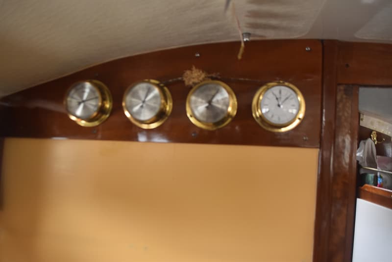 Vier ronde, goudkleurige meters met zilveren wijzerplaten en zwarte wijzers zijn gemonteerd op een houten paneel.