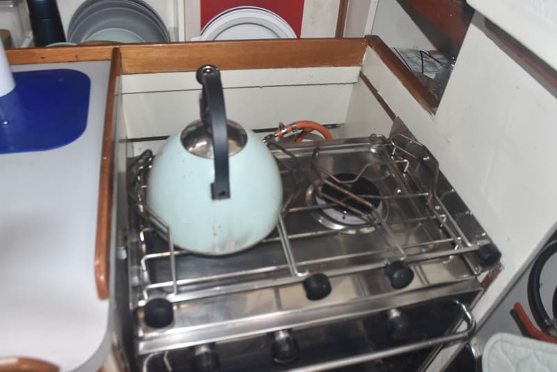 Een lichtblauwe waterkoker staat op een roestvrijstalen gasfornuis met twee pitten in een bootkeuken.