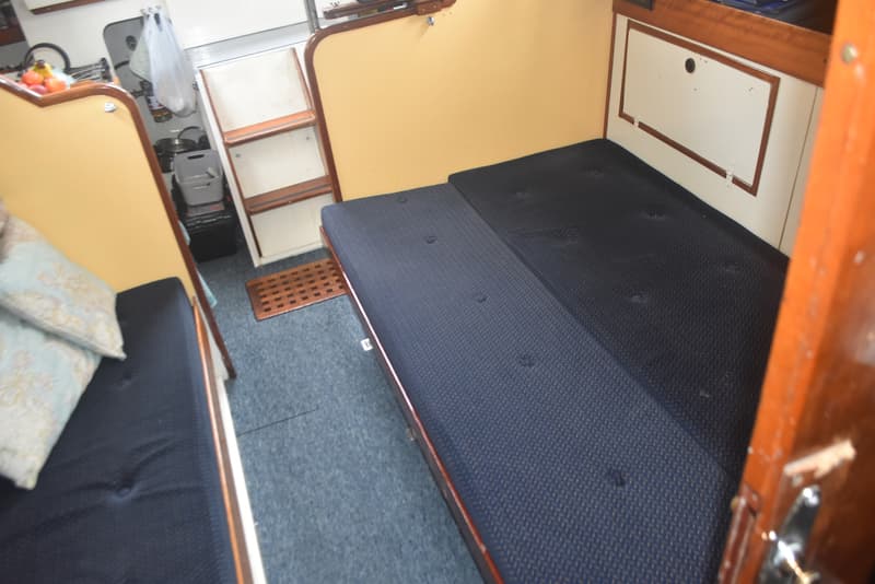 De foto toont een interieur van een boot met blauwe vloerbedekking, twee blauwe zitbanken en een houten trap.