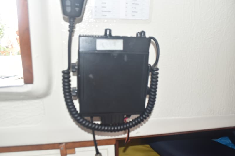 Een zwarte marifoon met een spiraalsnoer en microfoon hangt aan een witte wand, met een raam links.