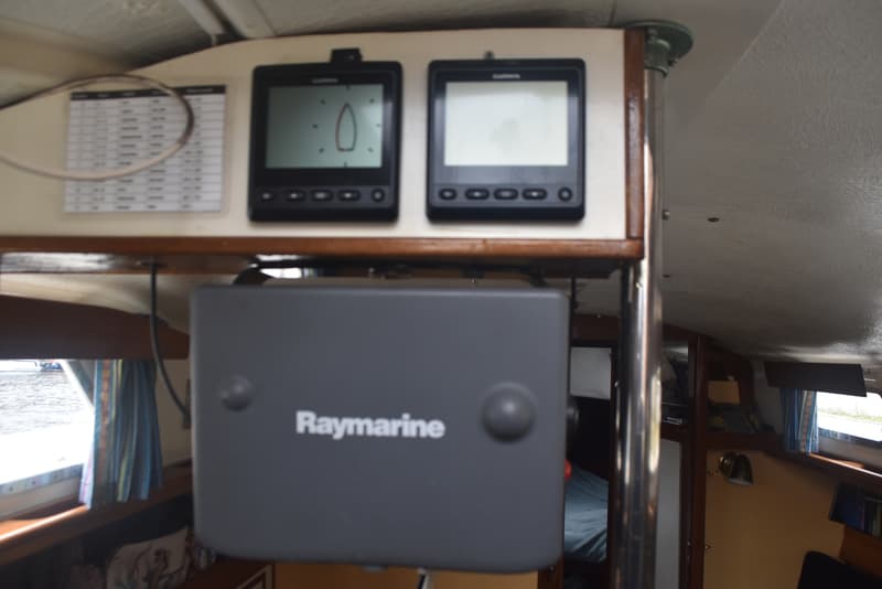 De foto toont een interieur van een boot met twee Garmin schermen, een Raymarine apparaat en een tabel aan de muur.