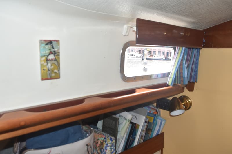 De foto toont een interieur van een boot met een patrijspoort, een schilderij en een boekenrek. — Frans Maas Raider 35