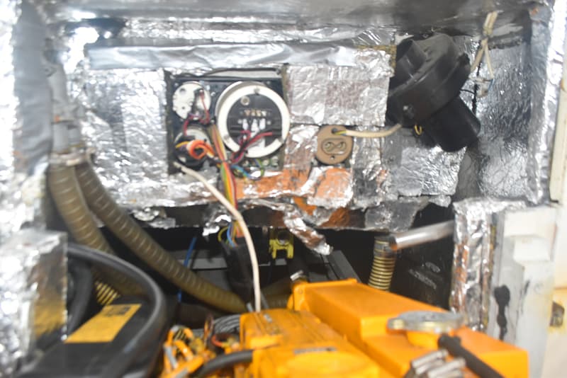 Een detailfoto van een motorruimte met een oranje motor, omringd door isolatiemateriaal en diverse kabels en slangen.