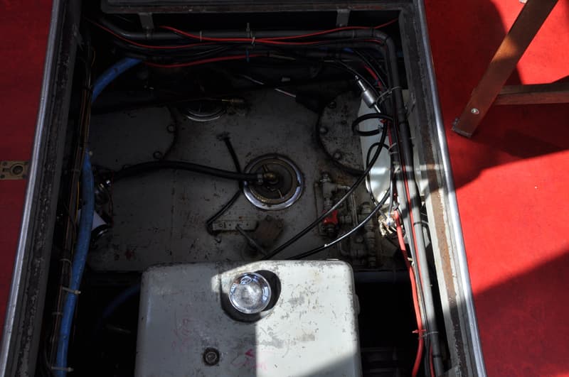 Een open luik toont een wirwar van kabels, leidingen en metalen onderdelen in een motorruimte.