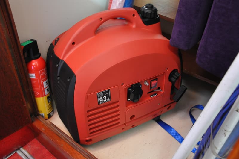 Een rode draagbare generator met een brandblusser ernaast en paarse kussens op de achtergrond.