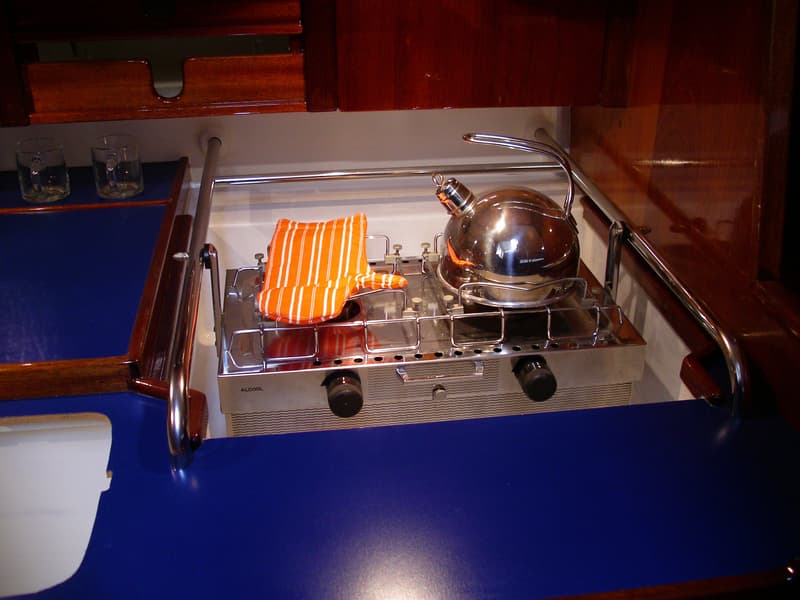 Een roestvrijstalen kooktoestel met twee pitten en een waterketel staat op een blauw aanrechtblad.