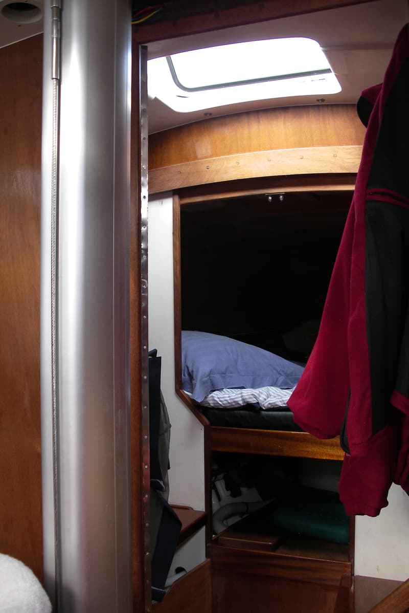 Een interieur van een boot met een bed, een patrijspoort en houten afwerking. — Waarschip 900 +