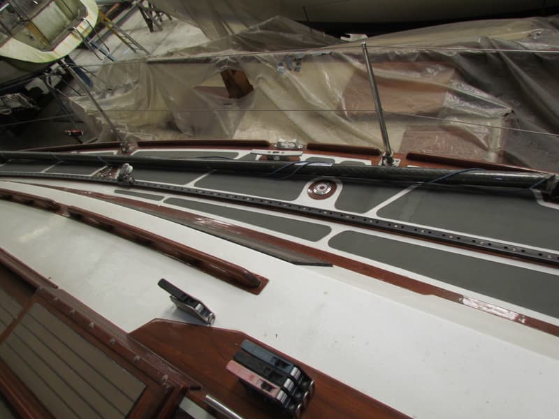 Een bovenaanzicht van een bootdek met houten accenten, grijze antislip en een deels afgedekte mast.