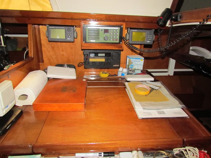 Een houten navigatiehoek met diverse apparatuur, een rol keukenpapier, een almanak en andere spullen.