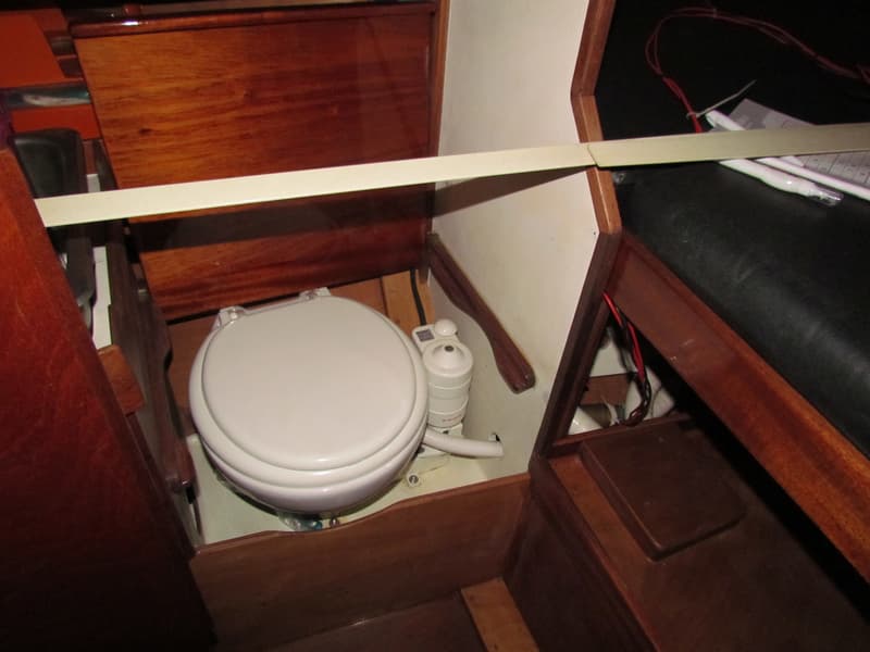 Een wit scheepstoilet met een pompmechanisme is zichtbaar in een houten interieur.