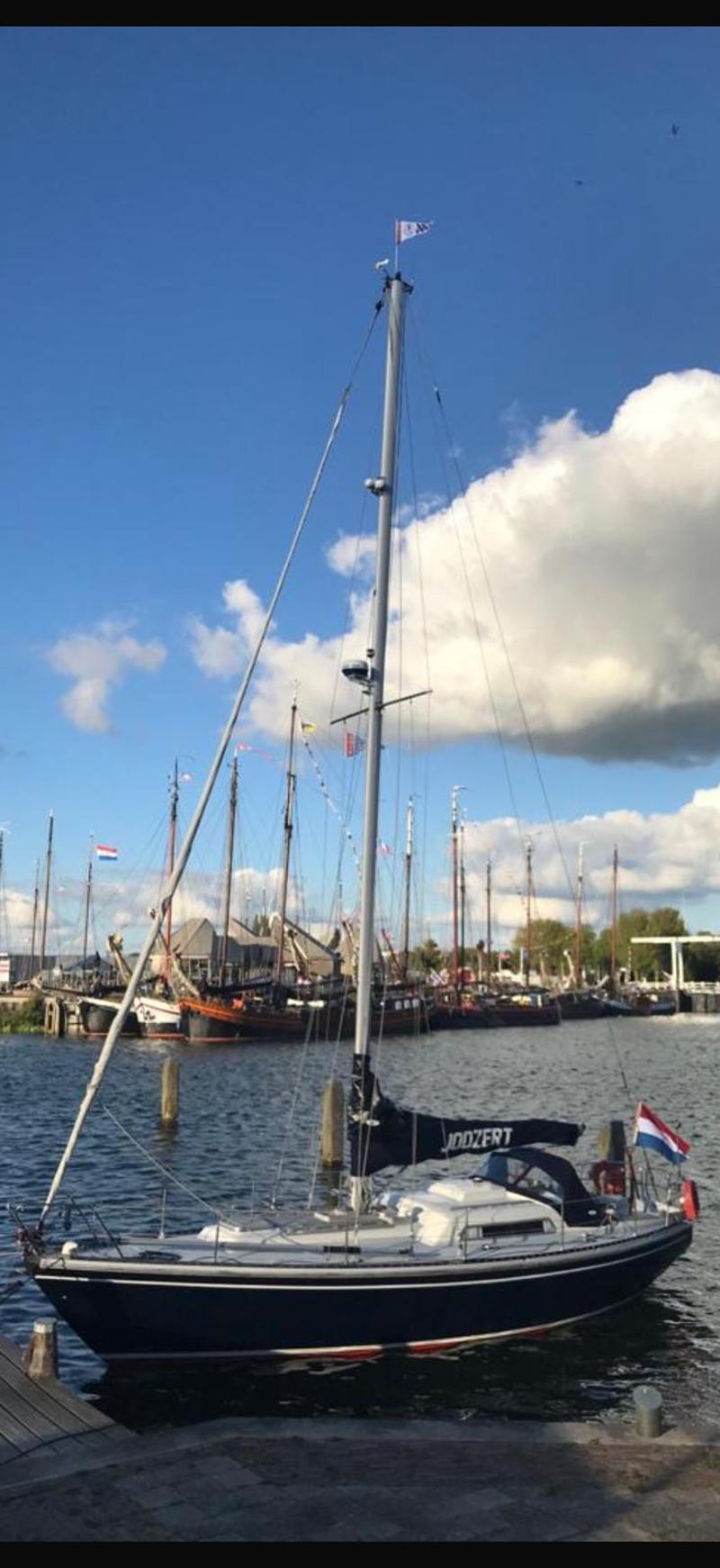 Een donkerblauwe zeilboot met een witte opbouw en een Nederlandse vlag, afgemeerd in een haven. — Victoire 34 Jodzert