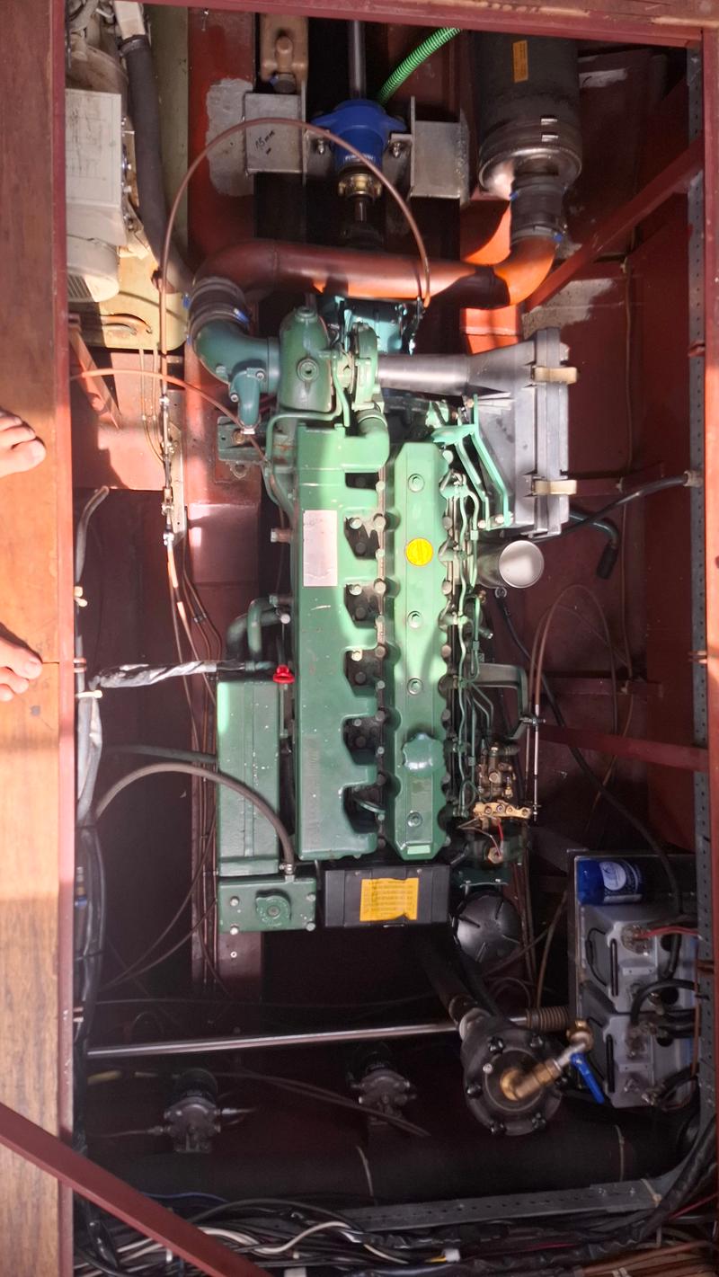 Een groene scheepsmotor met diverse slangen en kabels is zichtbaar in een donkere motorruimte.