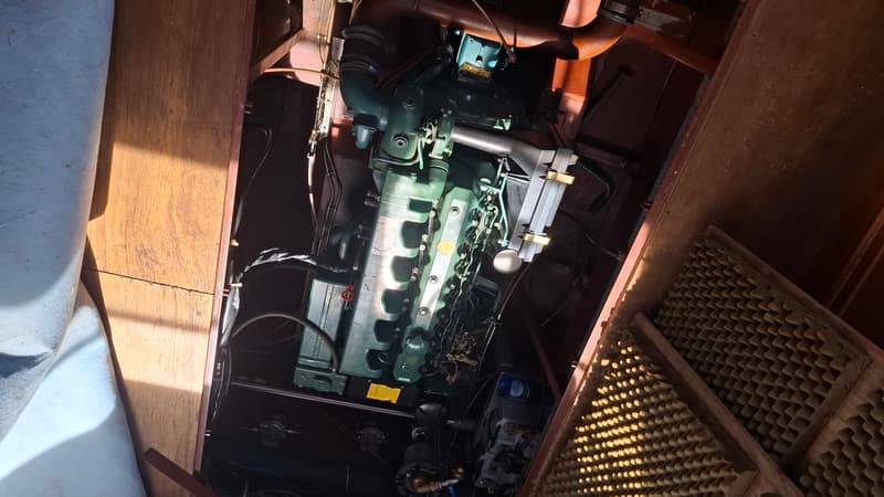 Een groene scheepsmotor is zichtbaar in een motorruimte met houten panelen en geluidsisolatie.