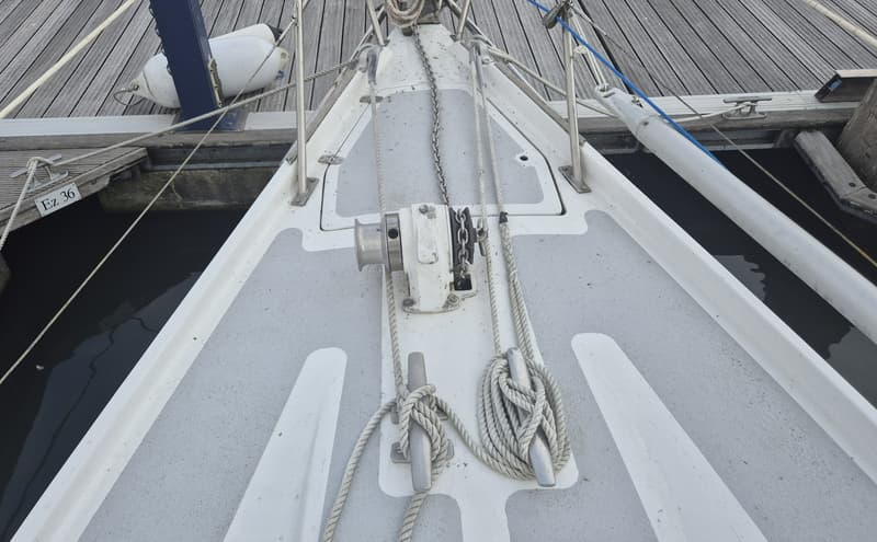 De boeg van een witte zeilboot met een ankerlier, touwen en kikkers, afgemeerd aan een houten steiger. — Contest 36 Ketch