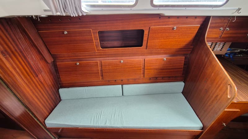 De foto toont een kajuitinterieur met houten wanden, kasten en een lichtblauwe gestoffeerde bank.