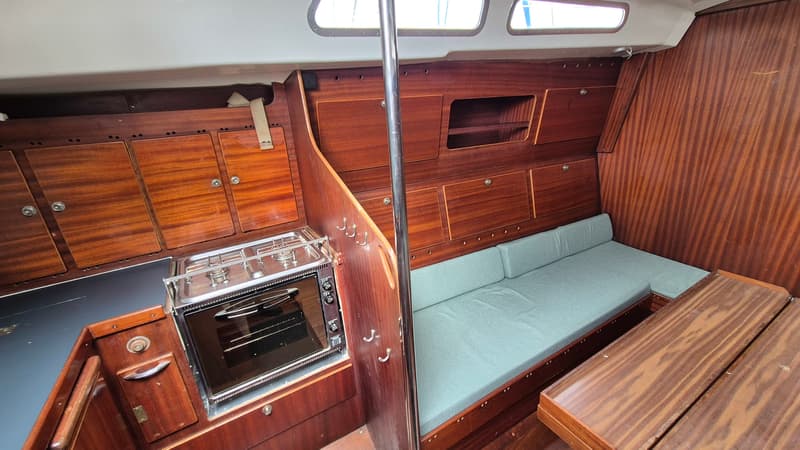 De foto toont het interieur van een boot met een kombuis, een bank met kussens en een houten tafel. — Contest 36 Ketch